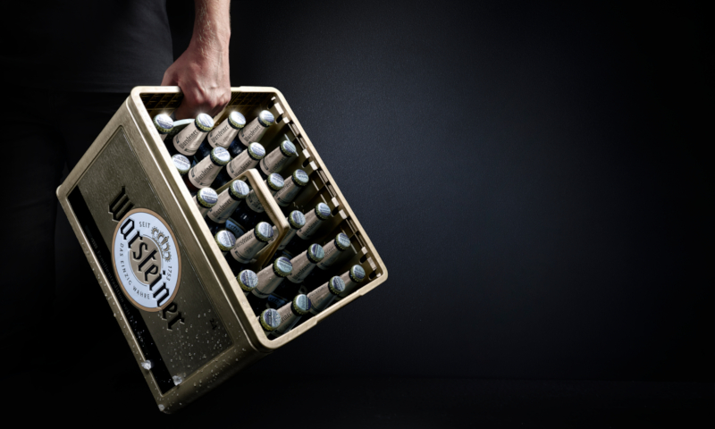 Nieuwe gouden Warsteiner krat wordt met één hand door iemand gedragen